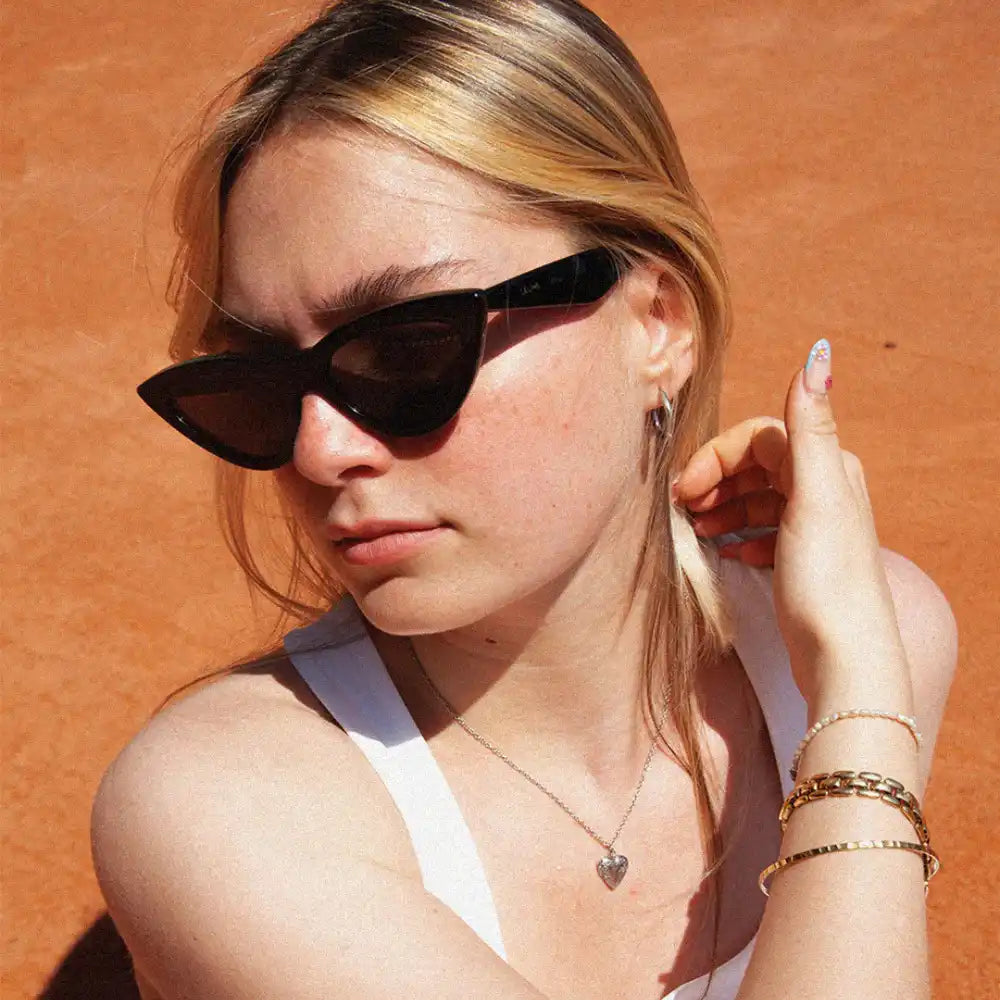 Une jeune femme portant des lunettes de soleil en forme de chat noir et plusieurs bracelets.