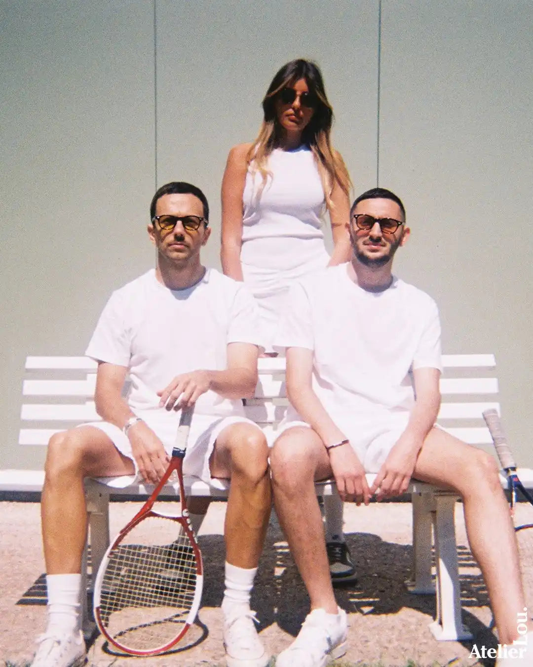 Trois personnes en tenue de tennis blanche avec des raquettes de tennis.